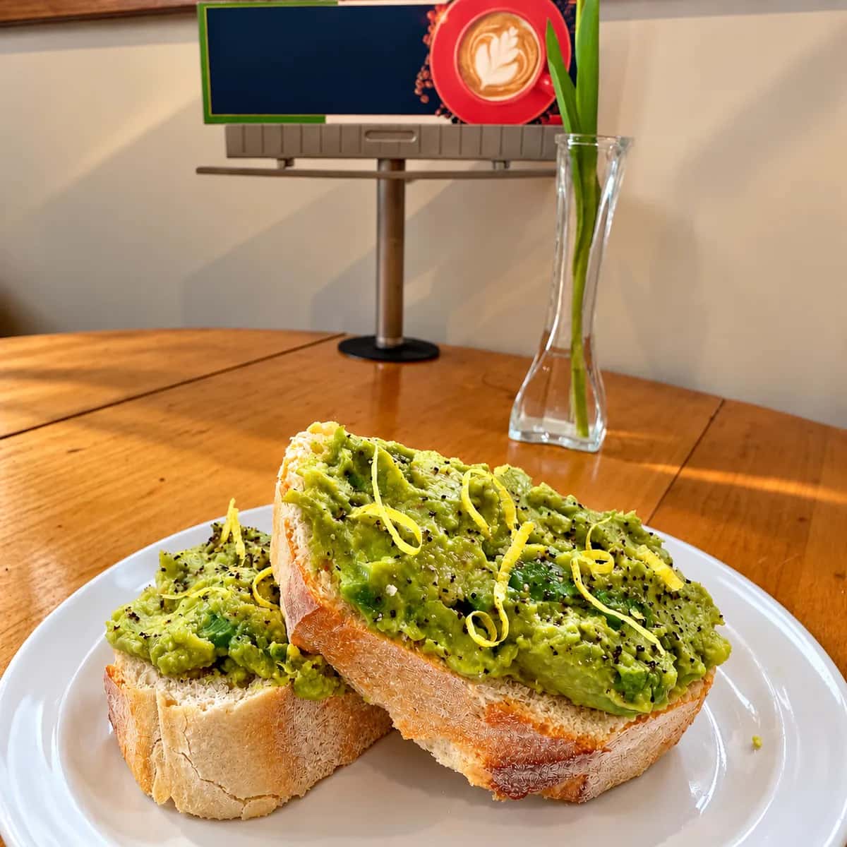 Two slices of toasted bread topped with mashed avocado, dark seeds and curls of lemon zest on a white plate