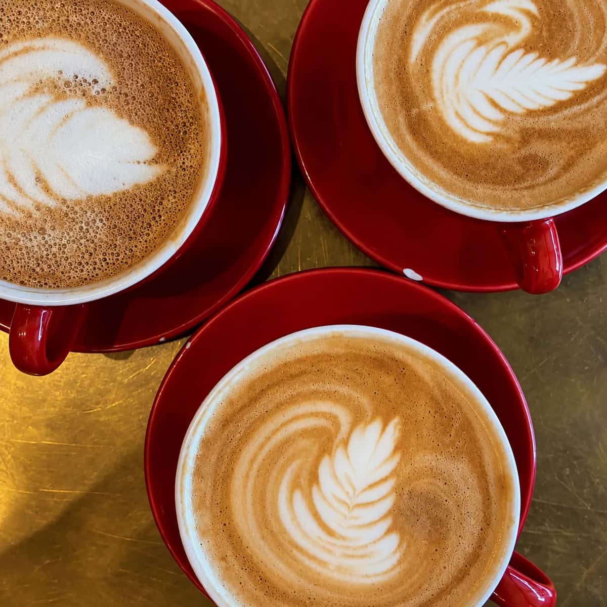 Three hot espresso drinks with rosetta latte art in red cups and saucers