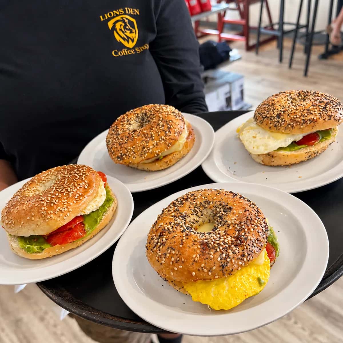 A tray of four bagel breakfast sandwiches carried by a Lions Den staff member